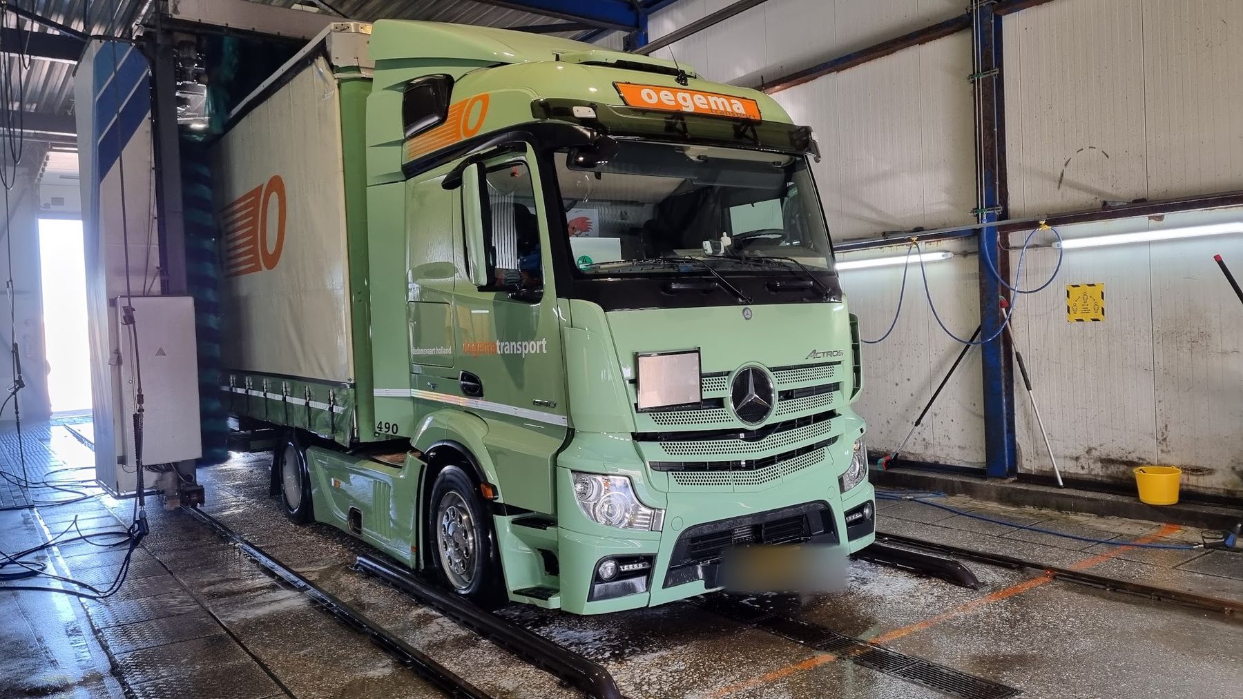 Een lichtgroene vrachtwagen met huifoplegger in de wasstraat