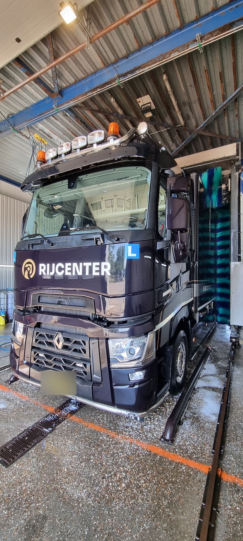 Een donkere vrachtwagen recht van voren onder het dak van de wasstraat